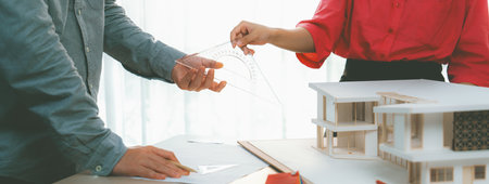 Young smart architect sends architectural equipment to project manager for measuring a house model and architectural equipment placed on meeting table. Creative design and teamwork. Variegated.の写真素材