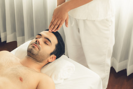 Caucasian man enjoying relaxing anti-stress head massage and pampering facial beauty skin recreation leisure in dayspa modern light ambient at luxury resort or hotel spa salon. Quiescentの写真素材