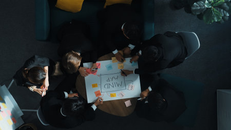 Top view of businesswoman write marketing idea on stick notes while standing near group of diverse people brainstorm financial strategy by using mind map. Start up team working together. Directorate.の写真素材