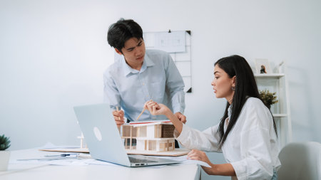 Professional male asian architect using ruler to measure house model length while young beautiful...