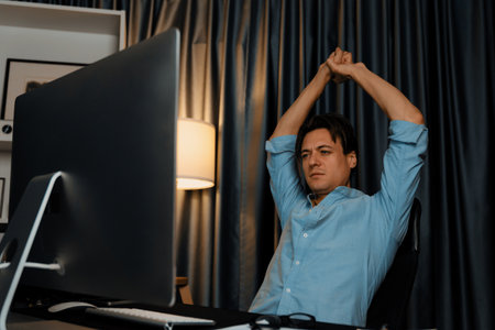 Sales manager working on desk with stretching arm up and down manner at night time at modern home...