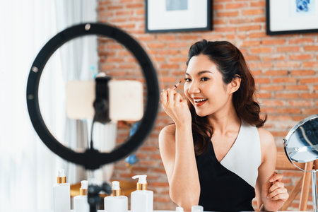 Woman influencer shoot live streaming vlog video review makeup uttermost social media or blog. Happy young girl with cosmetics studio lighting for marketing recording session broadcasting online.の写真素材