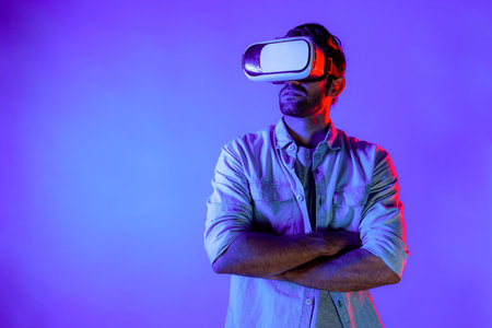 Smart caucasian man using virtual reality glass while crossing arm with confident. Professional happy teenager with casual cloth standing with folded arm colorful at neon light background. Deviation.の写真素材
