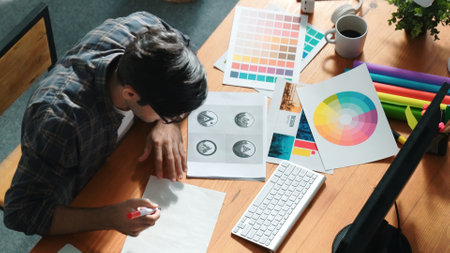 Interior designer looking at laptop and designing color while looking at palette at meeting table...