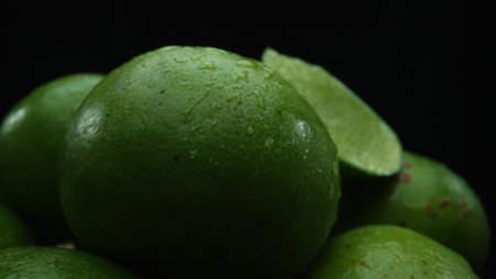 Slices of lime are meticulously arranged in a pile, set against a black background. Each lime slice is captured in stunning detail, its vibrant green hue and enticing texture. Close up. Comestible.の写真素材