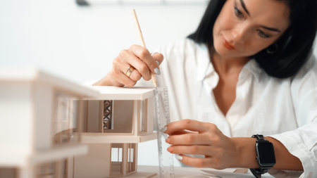 Closeup portrait image of professional young beautiful engineer architect using triangular scale measures house model with focusing at modern office. Business creative design concept. Immaculate.の写真素材