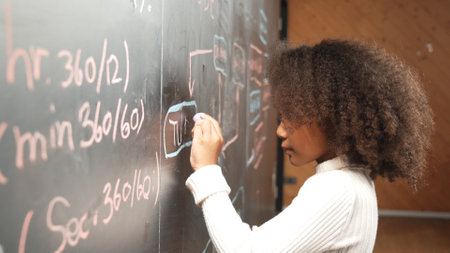 Site view of young african girl writing engineering prompt or code on blackboard. Skilled smart student planing a project by using coding and programing system in STEM technology classroom. Erudition.の写真素材