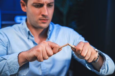 Stressful burnout of serious businessman destroying pencil for venting bad emotion in overwork load at night time. Concept of workload to solve issue problem at neon blue light of workplace. Sellable.の写真素材
