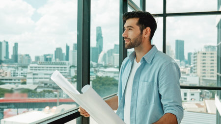 Professional architect engineer or male worker in casual outfit looking at skyscraper and city view while holding project plan. Creative design, civil engineering, building construction. Traceryの写真素材