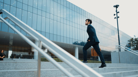 Skilled business man walking up stairs at park or city while holding bag in the hand Professional project manager going to workplace. Represent growth, getting promotion, increasing skill. Exultant.の写真素材
