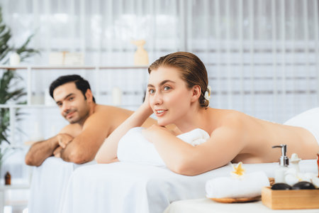 Blissful couple customer having exfoliation treatment in luxury spa salon with warmth candle light ambient. Salt scrub beauty treatment in health spa body scrub. Quiescentの写真素材