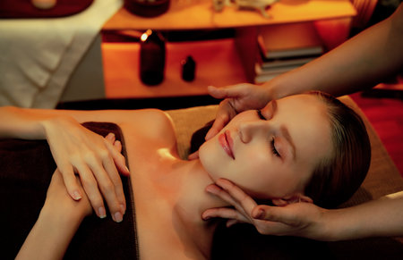 Caucasian woman enjoying relaxing anti-stress head massage and pampering facial beauty skin recreation leisure in warm candle lighting ambient salon spa in luxury resort or hotel. Quiescentの写真素材