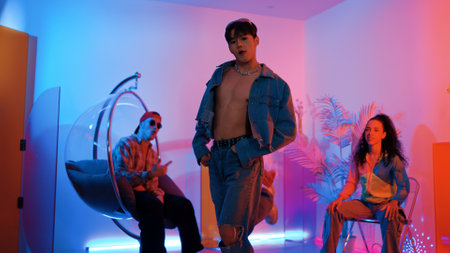 Skilled asian dancer moving to modern music while multicultural friend sitting at chair. Professional performer dancing show energetic foot step while hipster team cheering and supporting. Regalement.の写真素材