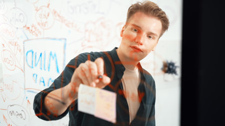 Closeup image of professional caucasian businessman presenting business idea with confident while writing and drawing mind map on glass board by using mind map and colorful sticky note. Immaculate.の写真素材