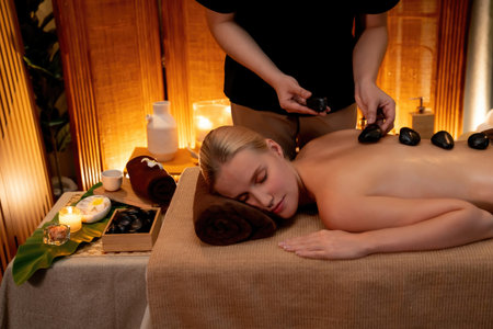 Hot stone massage at spa salon in luxury resort with warm candle light, blissful woman customer enjoying spa basalt stone massage glide over body with soothing warmth. Quiescentの写真素材