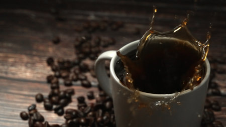 Falling drop in hot espresso in coffee cup decorated with piles of coffee bean placed on wooden...
