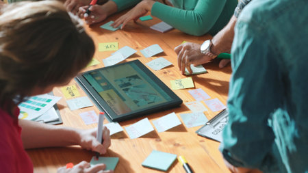 Top view of manager writing idea on sticky notes and explain idea about web design. Professional marketing team or programmer brainstorming idea while looking at tablet with color palette. Symposium.の写真素材