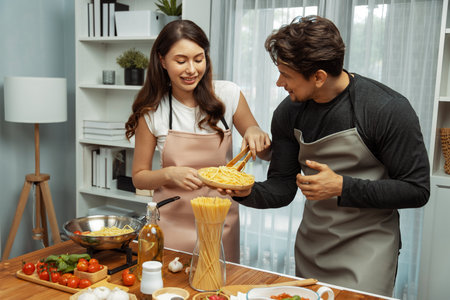 Couple chef influencers cooking special homemade of spaghetti with tongs taking to frying pan, putting seasoning and tasty sauce to make good flavor, recording on camera with live chanel. Postulate.の写真素材