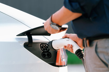 Young man put EV charger to recharge electric cars battery from charging station in city commercial...