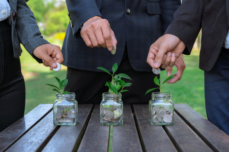 Business people put coin to money saving glass jar on outdoor table as sustainable money growth investment or eco-subsidize. Green corporate promot and invest in environmental awareness. Gyreの写真素材