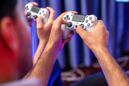 Close up of photo in holding joystick, playing video game or online streamer with friends in neon blue light curtain background. Concept of sitting couch lifestyles gamer in living room. Sellable.の写真素材