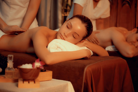 Caucasian couple customer enjoying relaxing anti-stress spa massage and pampering with beauty skin recreation leisure in warm candle lighting ambient salon spa at luxury resort or hotel. Quiescentの写真素材