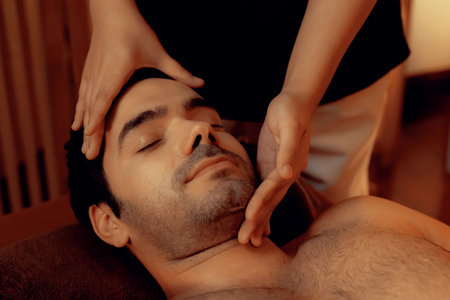 Caucasian man enjoying relaxing anti-stress head massage and pampering facial beauty skin recreation leisure in warm candle lighting ambient salon spa in luxury resort or hotel. Quiescentの写真素材