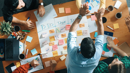 Top down aerial view of smart business team making scrum task board at meeting room. Group of smart people writing at paper and sticky notes for making kanban board and giving high five. Convocation.の写真素材