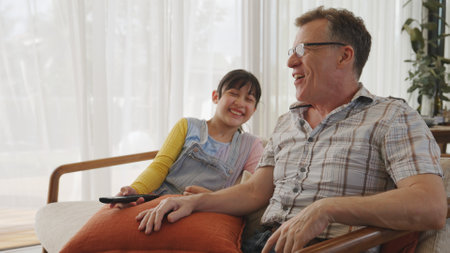 Grandfather and granddaughter together watch interesting entertainment media on TV. Old senior use technology communicate with young generation cross generation gap strengthen family bond. Divergence.の写真素材
