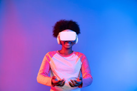 Young African wearing VR glasses through metaverse holding data learning application on blue pink...
