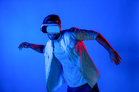 Happy man moving playing volleyball gesture movement while using VR glass at neon background. Caucasian teenager and gamer playing sport game while wearing goggle and innovation technology. Deviation.の写真素材