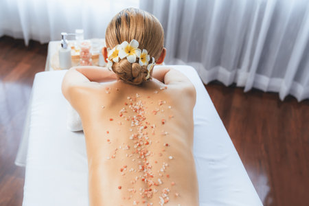 Woman customer having exfoliation treatment in luxury spa salon with warmth candle light ambient. Salt scrub beauty treatment in health spa body scrub. Quiescentの写真素材