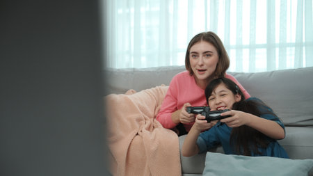 Happy girl playing game and sitting while mother lie on sofa. Caucasian parent and attractive smart...