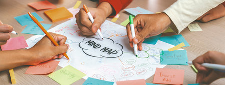 Professional startup group share creative marketing idea by using mind map. Young skilled business people brainstorm business plan while writing sticky notes. Focus on hand. Closeup. Variegated.の写真素材