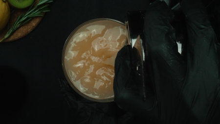 Top down view of skilled bartender hand prepare martini garnished with olive. Close up of hand making transparent cocktail drink with olive with movement and black background. Macrography. Comestible.の写真素材