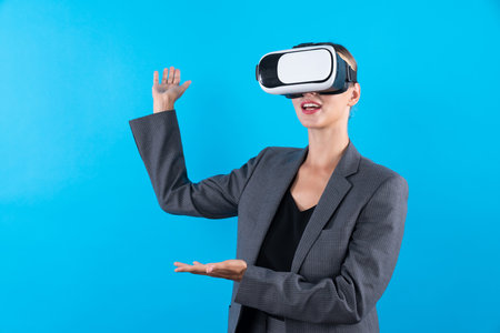 Businesswoman with VR glasses standing and present idea with confident while standing at blue background. Professional project manager wearing suit while holding something. Technology. Contraption.の写真素材