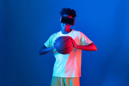 Young African American basketball gaming player wearing VR bouncing pose on blue pink neon light connecting digital futuristic technology virtual reality at metaverse world playing court. Contrivance.の写真素材