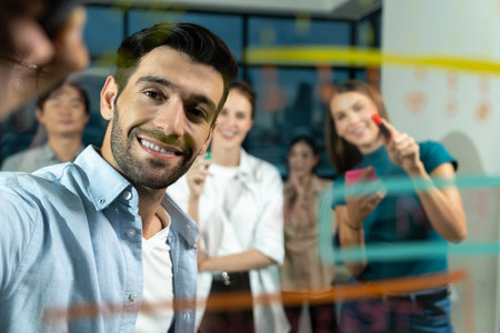Professional businessman writing on glass wall at night office while coworker listening carefully....