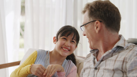 Grandfather and granddaughter together talking about entertainment media on TV. Old senior use...