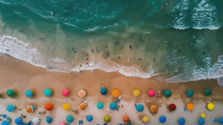 A birdseye view of a sandy beach adorned with colorful umbrellas, people enjoying the sun and water, against a backdrop of a vast blue sky AIG50の素材