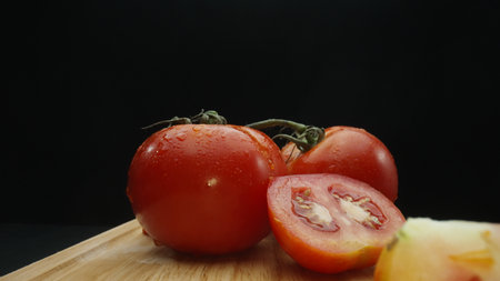 Macrography, slices of tomato rest elegantly on a rustic cutting board against a dramatic black...