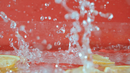 Close up of fresh lemon slices splashing on red background. Macro of sliced lemon dropping and falling in to splashing water. Freshness and hydration concept. Citrus. Design for poster. Pabulum.の写真素材