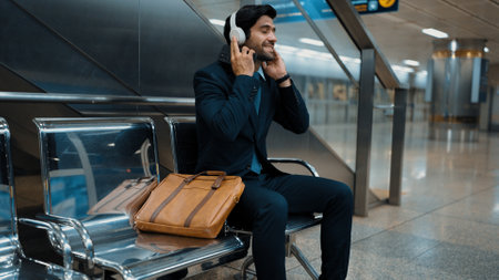 Skilled business man listening music while sitting at train station. Professional caucasian project manager waiting for train or subway. Male leader enjoy listen relaxed music with suit. Exultant.の写真素材