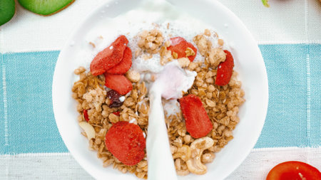 Close up of a white bowl of cereal with milk being poured into it. Top down aerial view of milk...