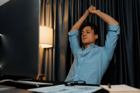 Sales manager working on desk with stretching arm up and down manner at night time at modern home office with monthly sales report for quarter presentation summary of profitable product. Pecuniary.の写真素材
