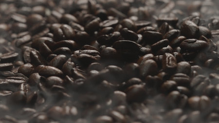 Close up of fresh brown coffee bean with roasted smoke from pile of coffee beans. Macrography of hot...