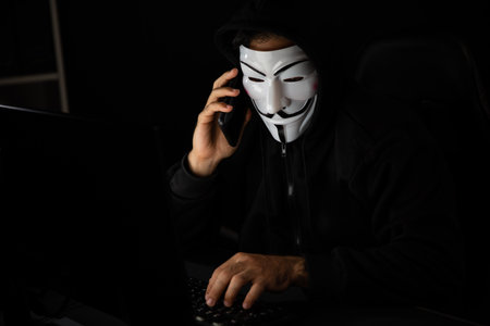 White smiling criminal anonymous mask calling to victim, convince to hack personal information, making share screen encryption program by hacker application on data server system in privacy. Surmise.の写真素材