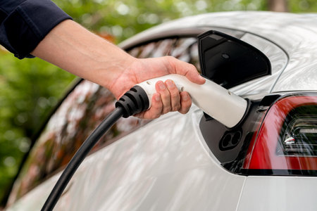 Man recharging battery for electric car during autumnal road trip travel EV car in autumnal forest. Eco friendly travel on vacation during autumn with electric vehicle. Exaltの写真素材