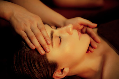 Closeup caucasian woman enjoying relaxing anti-stress head massage and pampering facial beauty skin recreation leisure in warm candle lighting ambient salon spa in luxury resort or hotel. Quiescentの写真素材