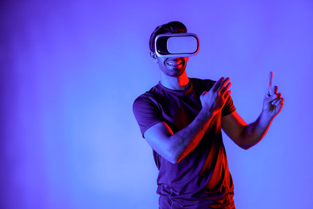 Caucasian man wearing virtual reality goggle while standing at neon light background. Person with VR goggle enter metaverse by using digital futuristic innovation technology while pointing. Deviation.の写真素材